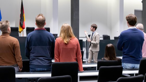 Bild: © Niedersächsischer Landtag Mehrere Besucherinnen und Besucher stehen mit dem Rücken zur Kamera und sehen sich im Forum des Niedersächsischen Landtages um, während ein Landtagslotse neben dem Redepult steht und in den Raum deutet.