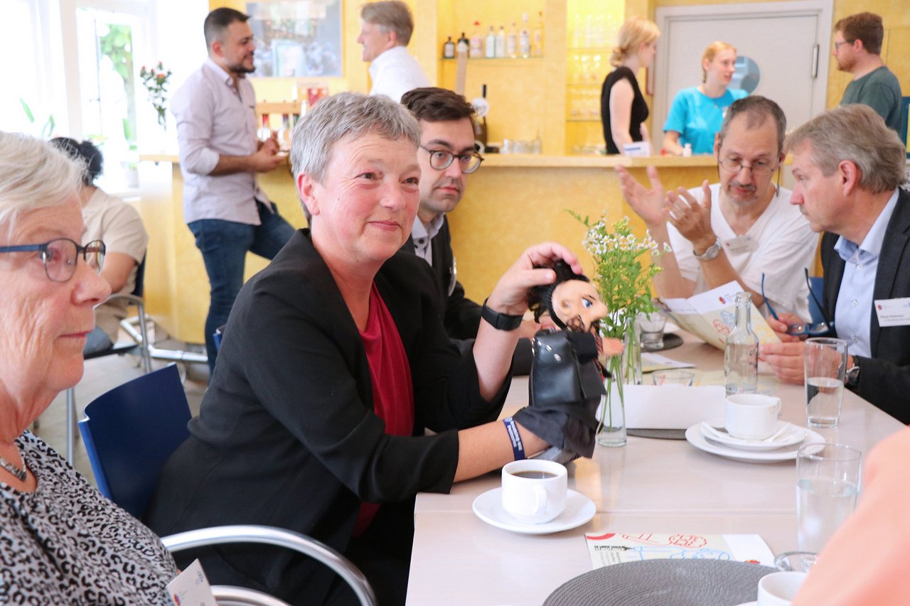 Landtagspräsidentin Naber mit anderen Personen an einem Tisch in lockerer Atmosphäre.