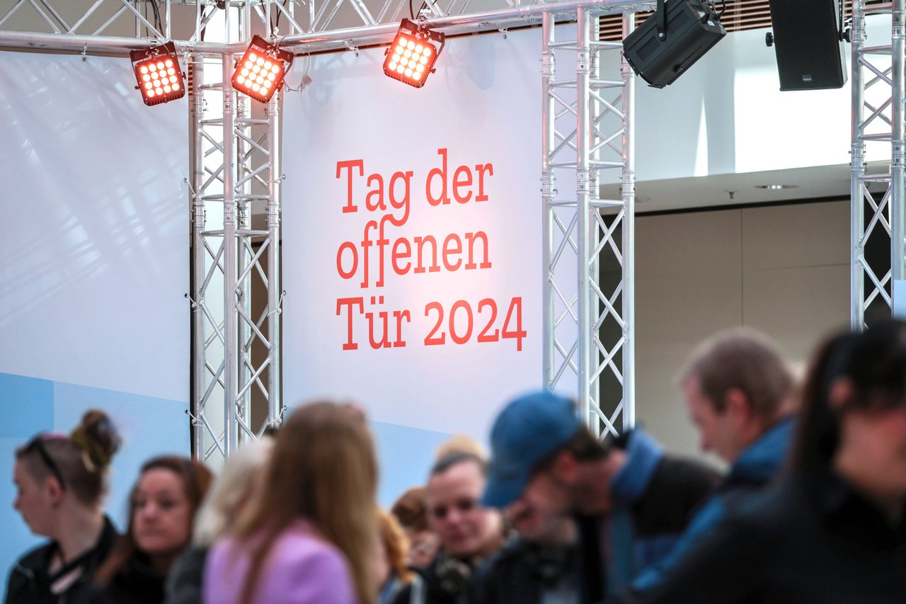 Schriftzug "Tag der offenen Tür 2024", im Vordergrund sind unscharf einige Menschen zu sehen.