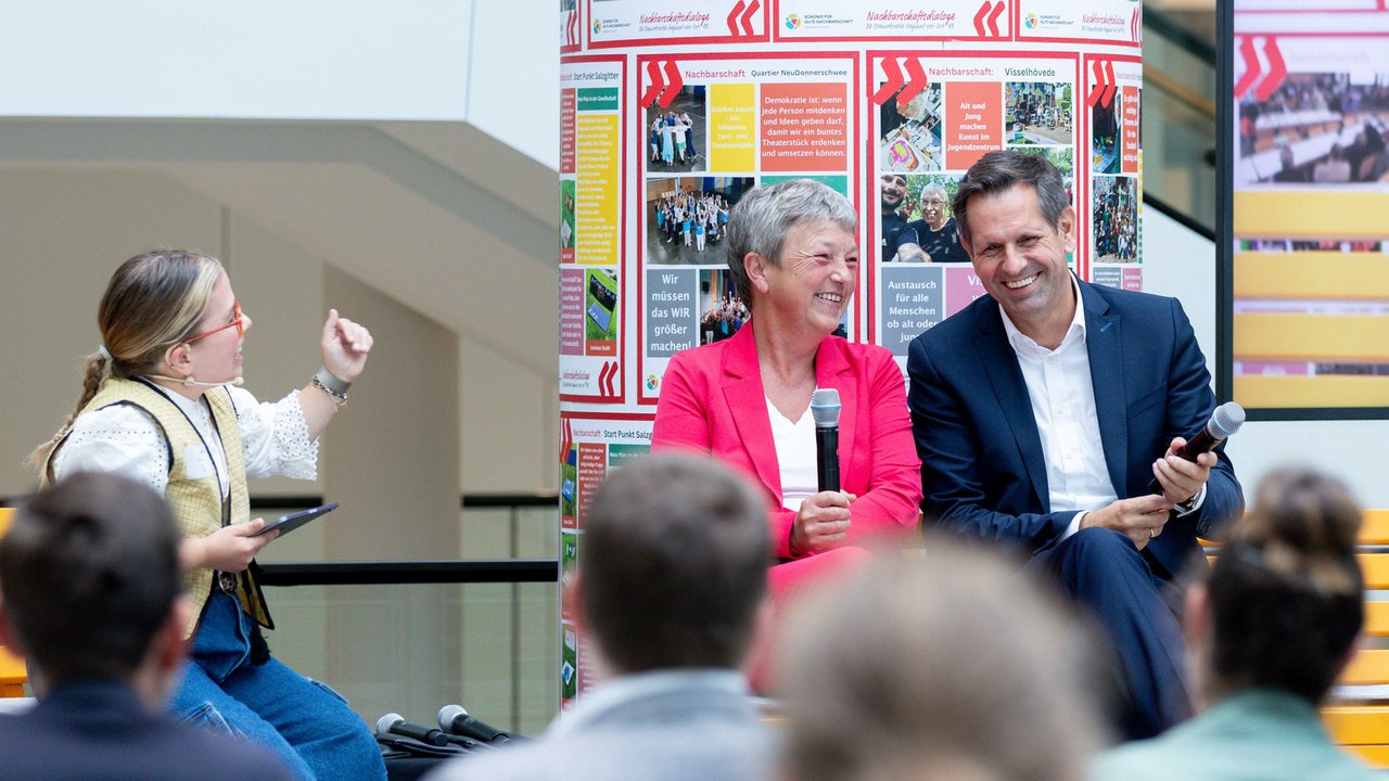 Landtagspräsidentin Hanna Naber und Minister Olaf Lies sitzen lachend neben der Moderatorin auf der Bühne. Im Vordergrund sieht man unscharf ein paar Hinterköpfe des Publikums.