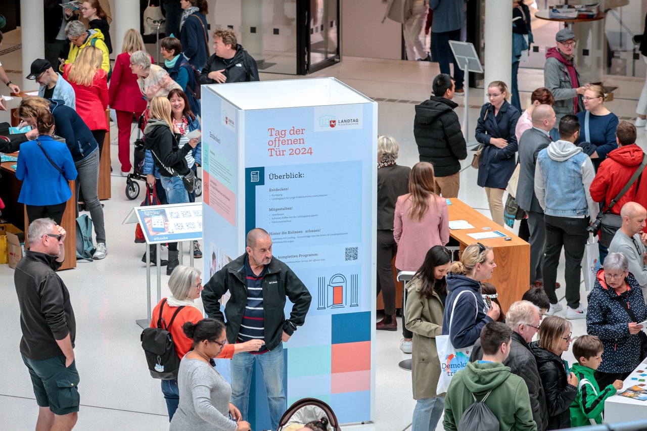 Ansicht der gut besuchten Portikushalle beim Tag der offenen Tür. In der Mitte steht eine Säule mit dem Text "Tag der offenen Tür 2024" sowie Informationen zum Programm.