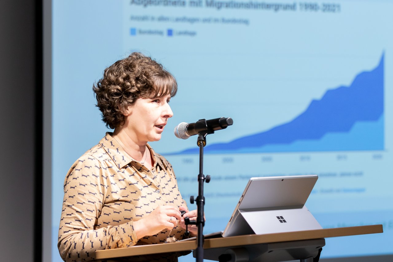 Seitliche Ansicht von Prof.in Dr.in Magda Nowicka am Redepult. Im Hintergrund ist ein Teil ihrer Präsentation zu sehen.